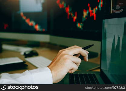 Employees analyze the graph of the stock market using a pen pointing to the computer screen.