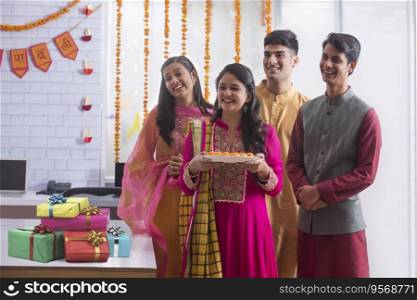 Employees standing together in office holding a plate of sweets during Diwali celebrations. 