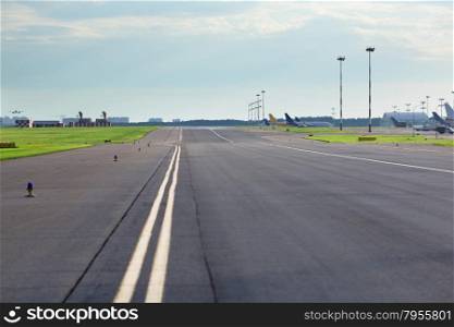 Empty airport asphalt runway with yellow marking, airplanes in the background