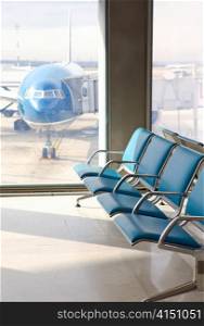 Empty armchairs in hall of expectation of airport and plane behind window