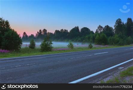 Empty asphalt road among flowering meadows under a clear blue sky in the early misty morning. Russian federal highway A119 in the White Nights season.