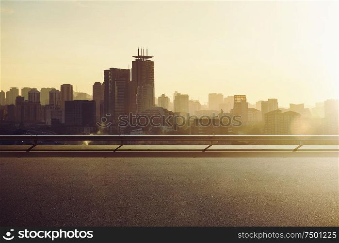 Empty asphalt road with city skyline background , sunrise or sunset scene .
