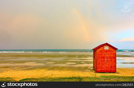Empty beach in low season with changing room and rainbow in the sky, Cyprus