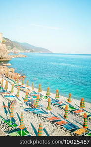 Empty beach with closed umbrellas on italian coast. Sunbeds and umbrellas at beautiful european seashore in Monterosso in Italy, Cinque Terre, Liguria