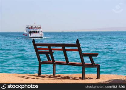 Empty bench near sea and shipped ship. Mass tourism at sea. Bench near beach. Departure of ship. Bench near beach. Unjustified expectations. Exotic relaxation. Holiday concept. Empty bench near sea and shipped ship. Mass tourism at sea. Bench near beach