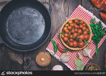 Empty black cast-iron frying pan and red cherry tomatoes in a wooden plate