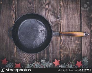 empty black cast-iron frying pan on a brown wooden background, top view