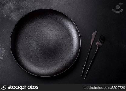 Empty black ceramic plate on a dark concrete background. Preparing the table for a family dinner