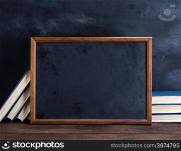 empty black chalk drawing frame and stack of books on a brown wooden table