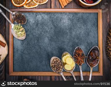 empty black chalkboard and spices in iron spoons on a brown wooden background