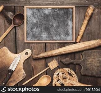 empty black frame and wooden kitchen vintage items  rolling pin, empty spoons , knife, cutting board on brown wooden table, top view