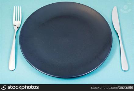empty black plate with fork and knife set on green background