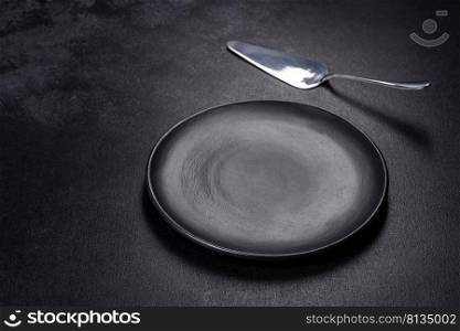 Empty black plates, fork and knife on a black background. Top view, copy space. Black plate on a black background. Flat lay, top view, copy space