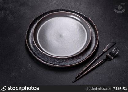 Empty black plates, fork and knife on a black background. Top view, copy space. Black plate on a black background. Flat lay, top view, copy space