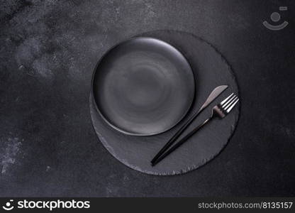 Empty black plates, fork and knife on a black background. Top view, copy space. Black plate on a black background. Flat lay, top view, copy space