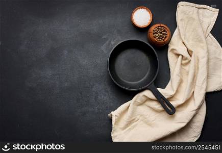 Empty black round cast iron frying pan with handle on black table, top view. Copy space