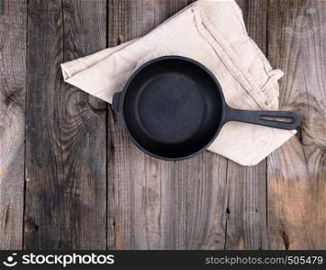 empty black round frying pan with handle and gray linen kitchen napkin on a gray wooden table, top view