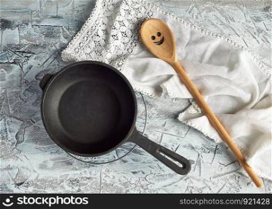 empty black round frying pan with handle and spoon on a cement background, top view