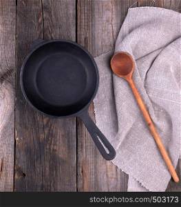 empty black round frying pan with handle and spoon on a wooden table, top view