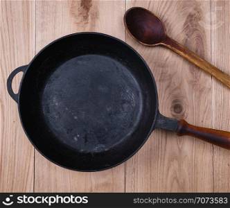 empty black round frying pan with wooden handle on a wooden table, top view