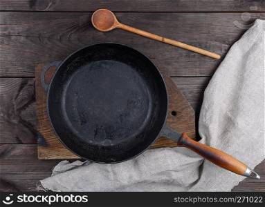 empty black round pan with wooden handle and wooden spoon on a brown table, top view