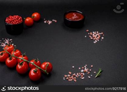 Empty black texture table, cherry tomatoes on a twig, spices, salt and herbs. Ingredients for cooking at home