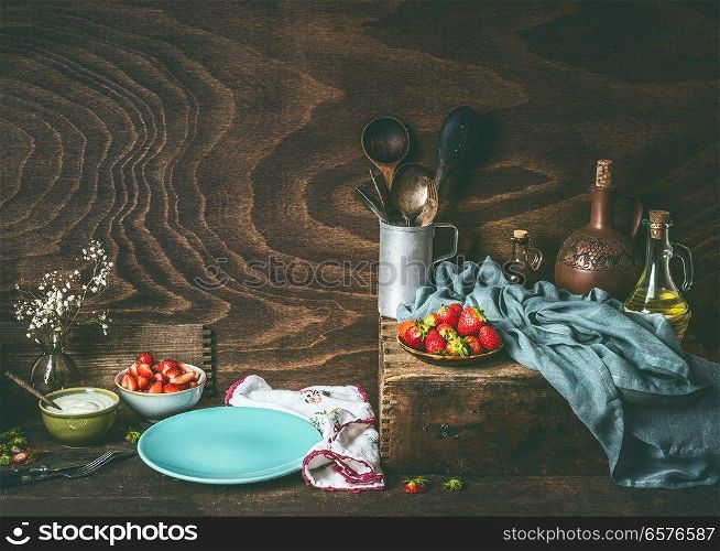 Empty blue plate on dark rustic wooden kitchen table with strawberries and yogurt in bowls. Country style food background , still life, front view. Place for your design, recipes , text or products
