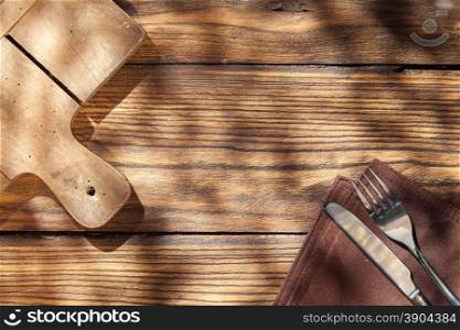 Empty board with fork and knife on wooden table. Top view