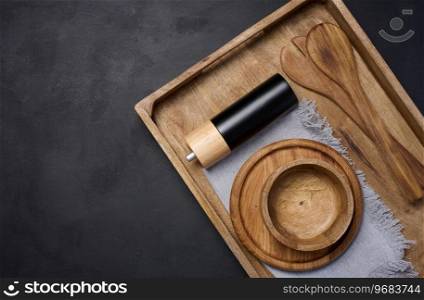 Empty bowl and wooden spoons on a black table, top view. Copy space