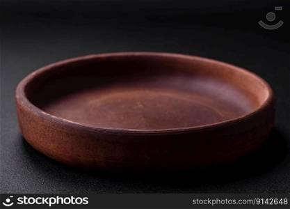 Empty brown colored ceramic plate on dark textured concrete background. kitchen utensils