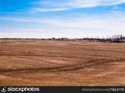 Empty brown farm fields with barn in distance against partly cloudy sky.