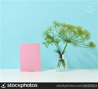 empty cardboard pink sheet of paper and glass vase with a bouquet of dill on a white table. Minimalism in the interior