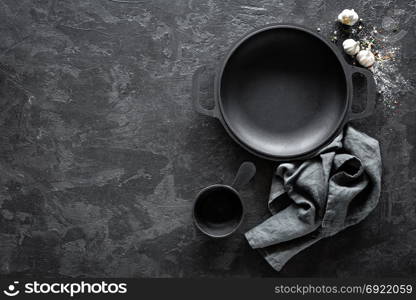 Empty cast-iron pan on dark background for restaurant menu, top view. Empty cast-iron pan with cutlery on dark background for restaurant menu, top view