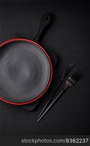 Empty ceramic plate on dark textured concrete background. Cutlery on the kitchen table