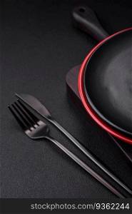 Empty ceramic plate on dark textured concrete background. Cutlery on the kitchen table