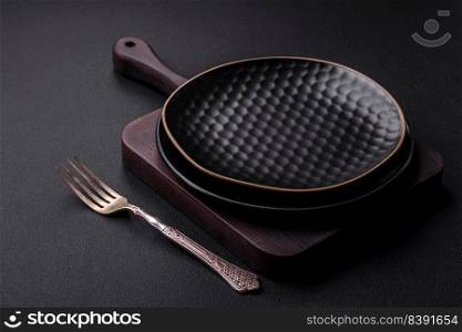 Empty ceramic round plate on dark textured concrete background. Cutlery, preparation for dinner
