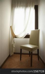 Empty chair by window with drapes in Venice, Italy.