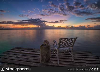 Empty chair on a wooden pier waiting for sunrise on the sea beach.