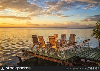Empty chairs and table on a wooden pier at amazing colorful sunrise in the sea.