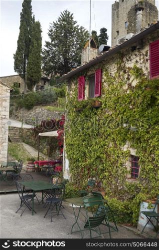 Empty chairs and table on sidewalk cafe by house with ivy plants, Chianti, Tuscany, Italy