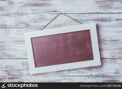 Empty chalkboard on the rope attached to shabby white wooden background. Empty chalkboard