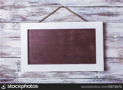 Empty chalkboard on the rope attached to shabby white wooden background. Empty chalkboard