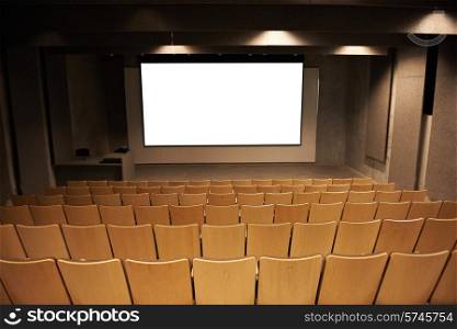 Empty cinema with white isolated screen and brown chairs.