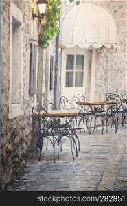 Empty coffee terrace with tables and chairs in old town of Budva, Montenegro. Vintage style photo