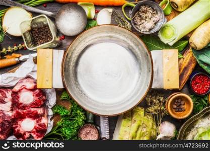 Empty cooking pot with cooking ingredients for meat soup or broth on kitchen table, top view