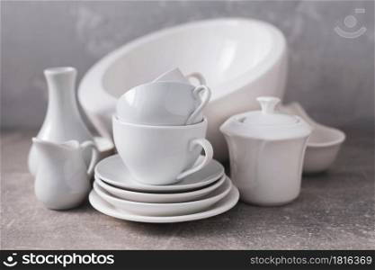 Empty crockery set or white ceramic dishes. White kitchen dishware and tableware on table near grey wall background texture