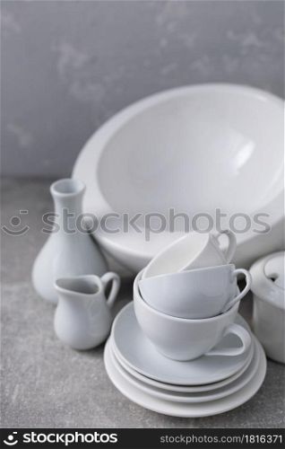 Empty crockery set or white ceramic dishes. White kitchen dishware and tableware on table near grey wall background texture