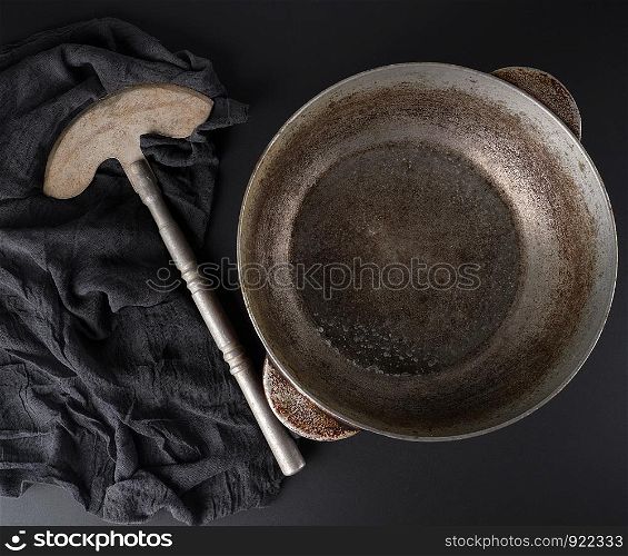 empty crooked vintage aluminum stewpan and old knife on a black background with black gauze fabric, top view