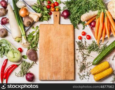Empty cutting board and various raw vegetables for tasty and healthy cooking, top view, place for text, frame. Vegan or vegetarian food concept