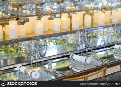 empty dishware set and candles in restaurant with long table. in a row dishware and candles in front of the mirror. empty dishware  on a long table